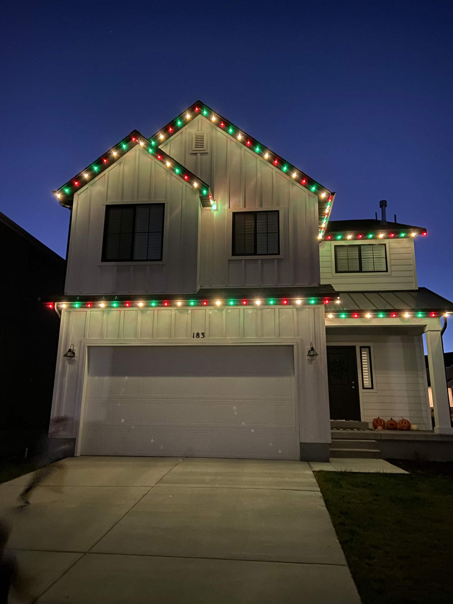 Modern farmhouse two-story home with red, green and warm white roofline lighting at dusk