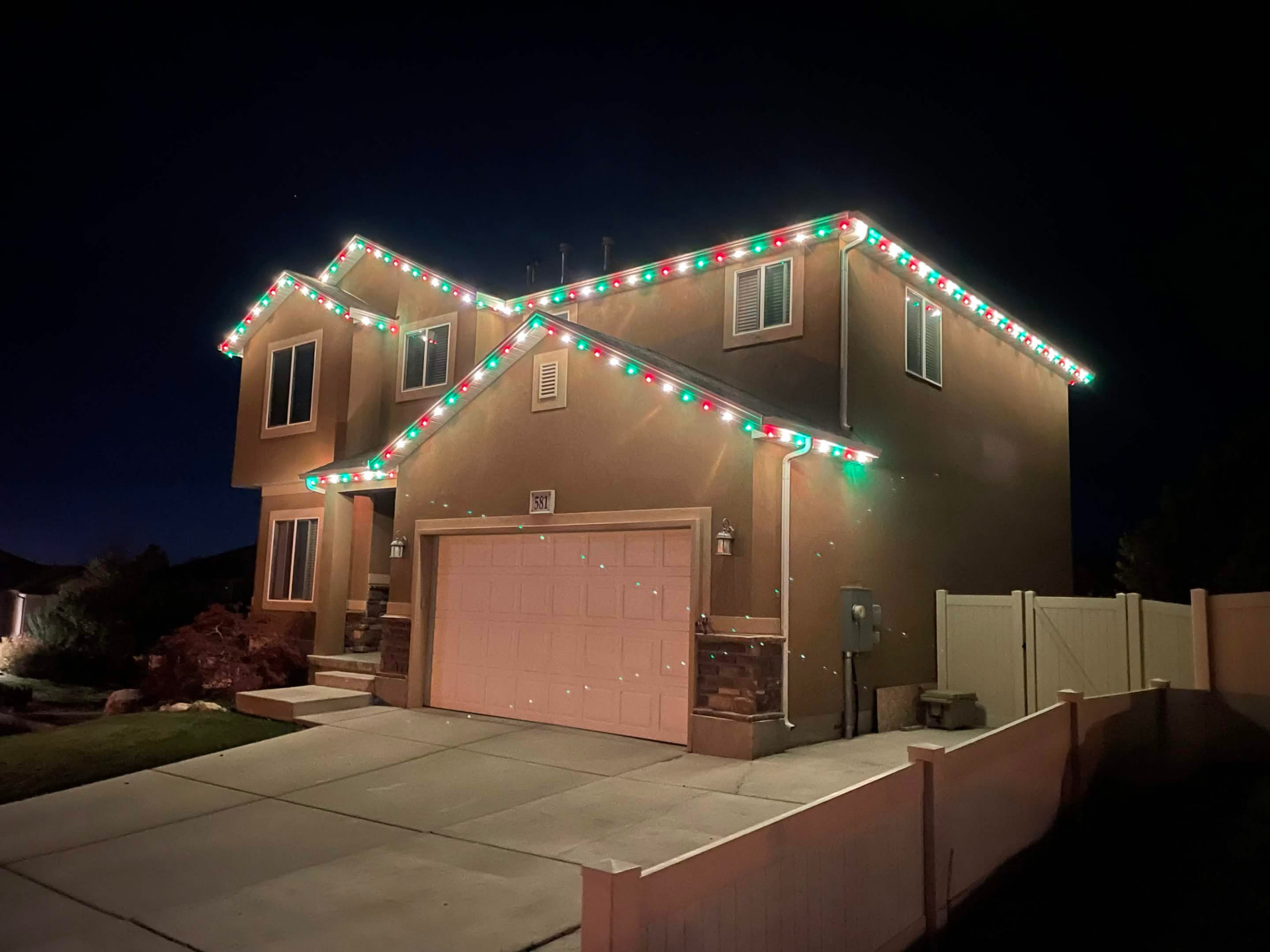 Two-story stucco Utah home with red, green and white Christmas roofline lighting