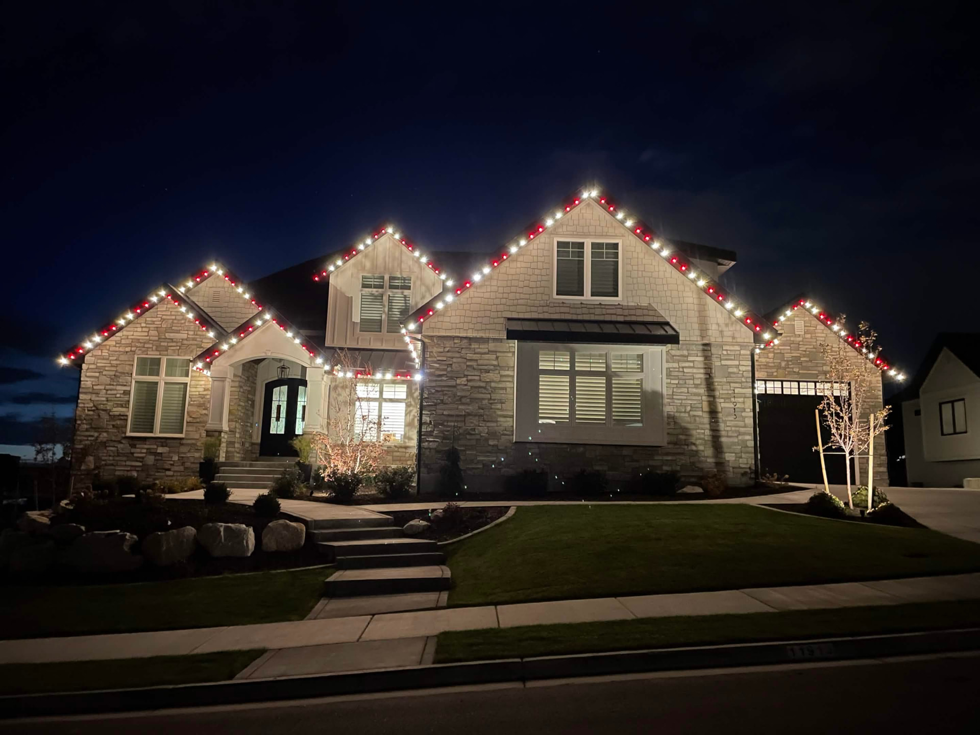 Stone and shake Utah home outlined in red and warm white C7 Christmas roofline lighting