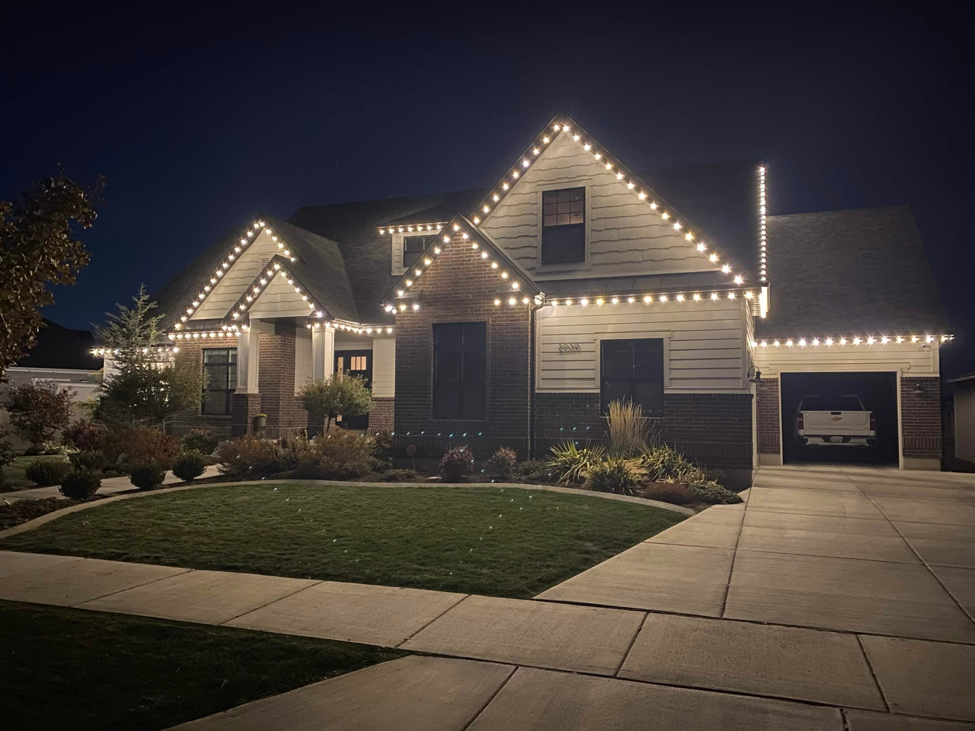 Large Utah brick home at night with warm white roofline and landscape lighting installed by Level Up Lighting